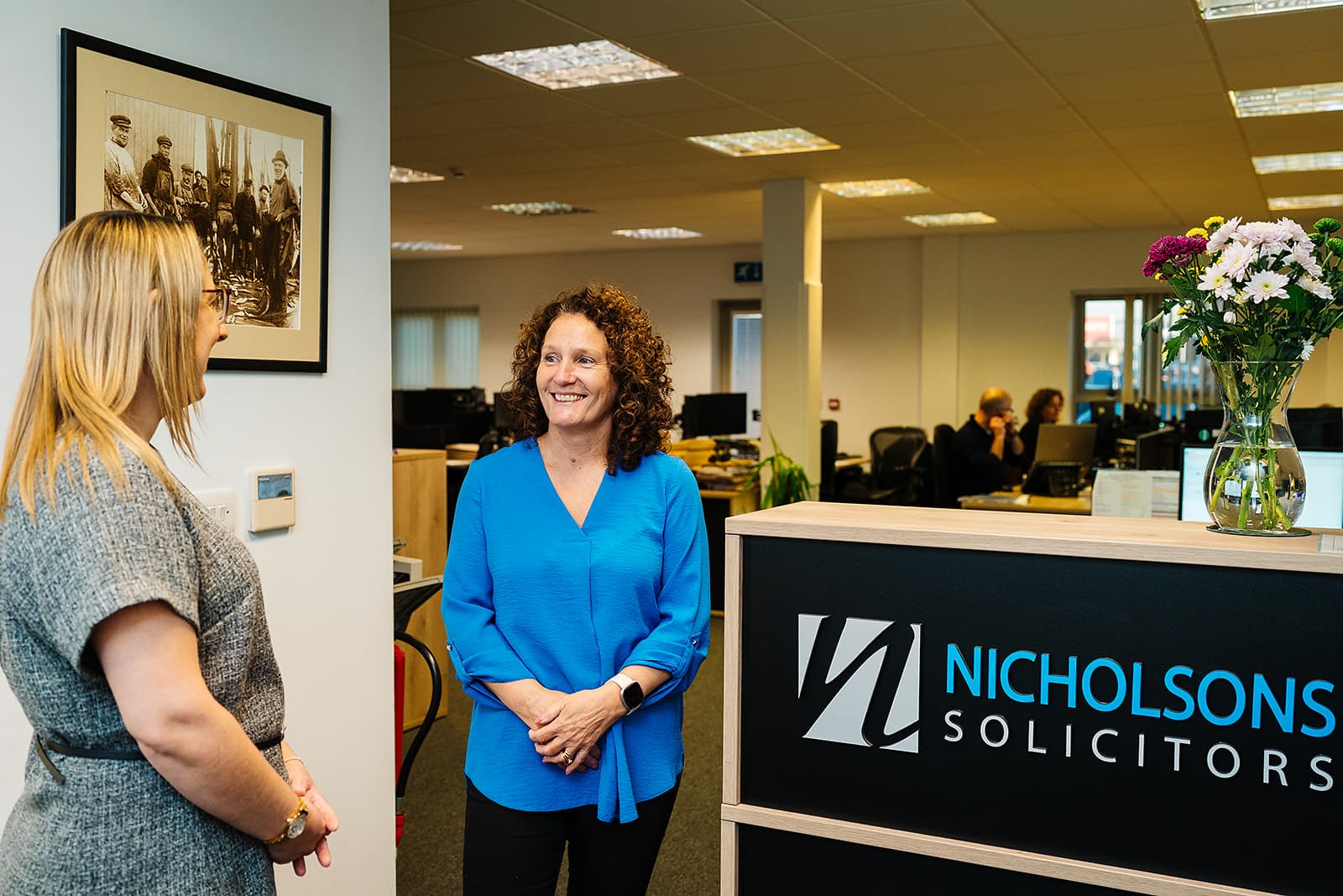 Two colleagues talking beside the Nicholsons Solicitors reception desk in the open-plan office — contractual dispute solicitors in Lowestoft and Norwich